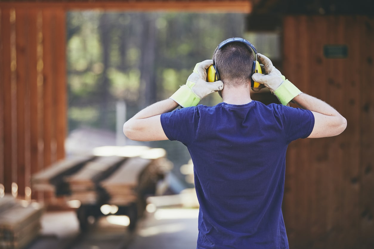 Man working at a sawmill putting on hearing protection.