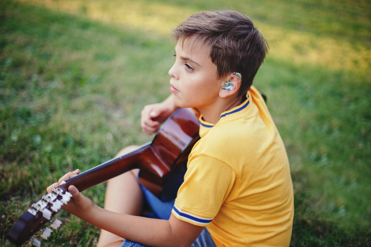Young boy with hearing aids plays guitar