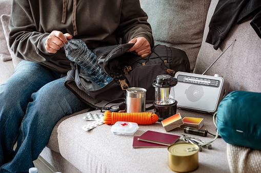 Woman filling emergency backpack with disaster emergency supplies. Preparing for crisis or disaster.