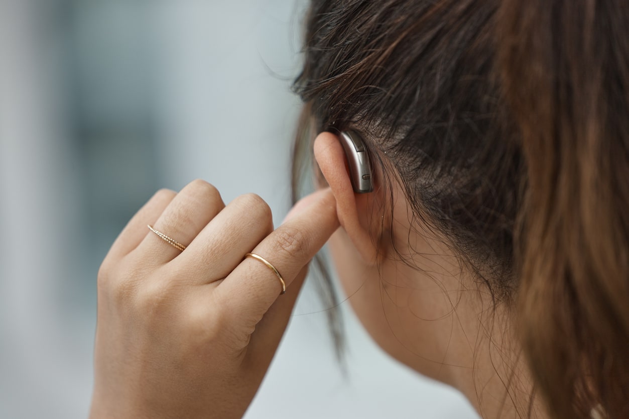Closeup of a woman touching her ear with a hearing aid in it.