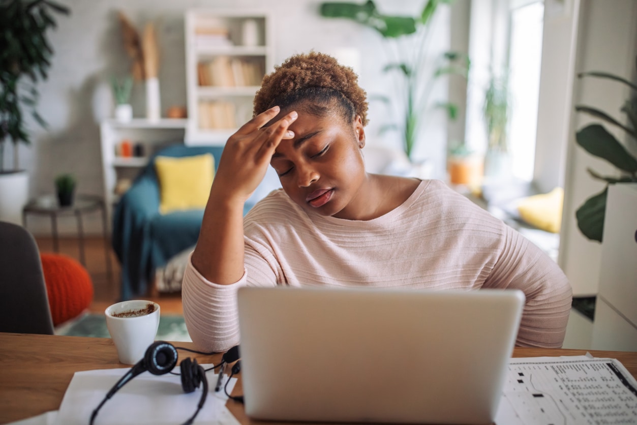 Tired woman rubbing her forehead, looking at her computer.