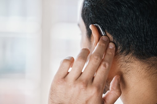 Back view of a man touching his hearing aid.
