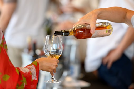 Bartender pouring rose wine for tasting, woman is holding her wineglass to fill it.