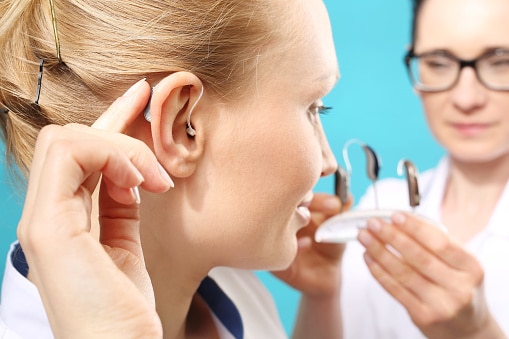 Young woman trying on a hearing aid. Specialist holding a few other hearing aid options in the background.